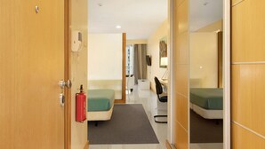 Een hotelkamer met een bed, een bureau, een stoel, een brandblusser en een spiegel.