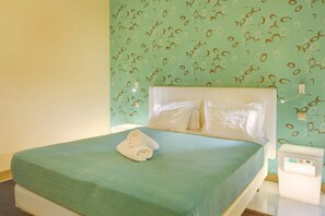 Una cama con una colcha verde, almohadas blancas y una toalla enrollada.