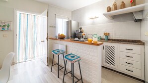 A modern kitchen with a central island, bar stools, a refrigerator, and a window with curtains.
