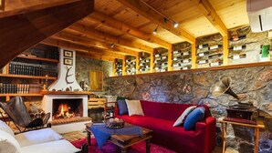 A cozy living room with a fireplace, a red sofa, and a bookshelf filled with books and wine bottles. - Pine Forest Chalet 1400m | Cinema & Fireplace (Artemisia)