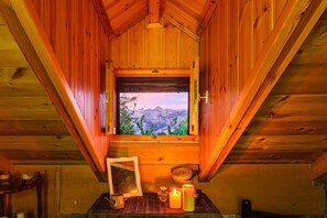 A wooden cabin with a window offering a mountain view, a framed picture, candles, and a small table. - Pine Forest Chalet 1400m | Cinema & Fireplace (Artemisia)