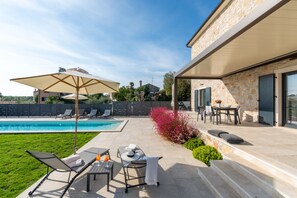 A poolside area with lounge chairs, a table, and an umbrella.