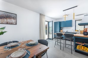 Uma cozinha moderna com armários azuis, uma mesa de jantar de madeira posta com pratos e copos, e vista para o exterior por uma porta de vidro.