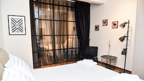 A hotel room with a large bed, a chair, a small table with a plant, and a floor lamp. - Central apartment at Echarxia 2 beds for 5 pers by MPS (Αθήνα)