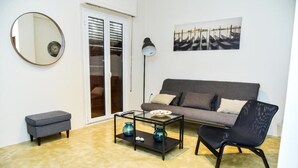 A living room with a grey sofa, a black chair, a glass coffee table with decorative vases, a round mirror, and a painting on the wall. - Central apartment at Echarxia 2 beds for 5 pers by MPS (Αθήνα)