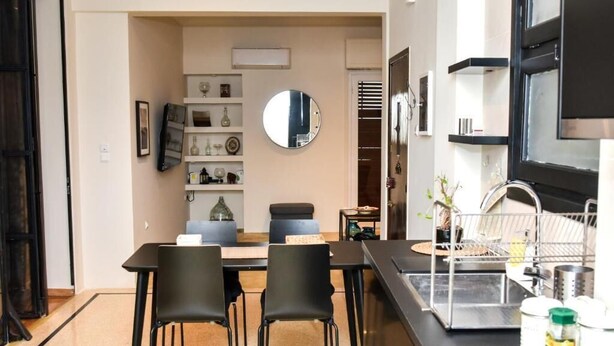 A modern kitchen with a black countertop, a stainless steel sink, and a dining area with a table and chairs. - Central apartment at Echarxia 2 beds for 5 pers by MPS (Αθήνα)