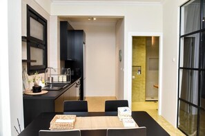 Une cuisine moderne avec des meubles noirs, un coin repas avec une table et des chaises, et une vue sur une salle de bain équipée d’une douche et de toilettes.