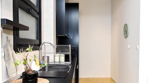 A modern kitchen with a black countertop, a woven placemat, a potted plant, a metal rack, and a clock on the wall. - Central apartment at Echarxia 2 beds for 5 pers by MPS (Αθήνα)