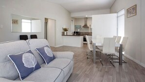 Una sala de estar moderna con sofá, una mesa de comedor con sillas, una zona de cocina y un espejo grande.
