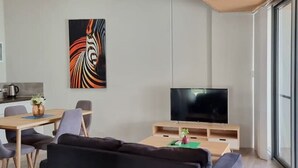 A modern living room with a black sofa, a wooden coffee table, a flat-screen TV, and a painting on the wall. - Waverley apartment D-one bedroom, wifi available (Beckenham)