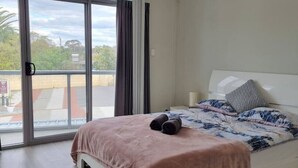 A bedroom with a large sliding glass door leading to a balcony, a bed with a pink blanket, and a patterned bedspread. - Waverley apartment D-one bedroom, wifi available (Beckenham)