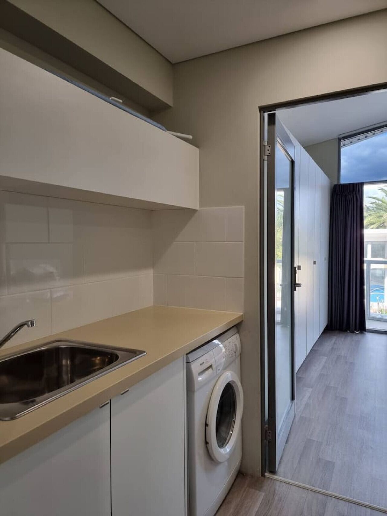 A modern kitchen with a built-in washing machine, a sink, and a sliding glass door leading to a balcony.
