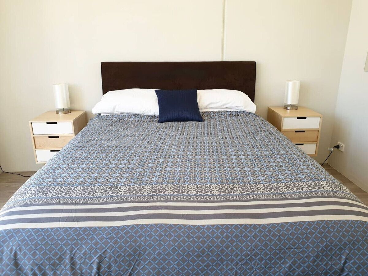 A bed with a patterned bedspread, two bedside tables with lamps, and a wooden headboard.