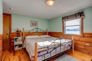 Un dormitorio con estructura de cama de madera, una mesita de noche, una ventana con cortinas y un cuadro enmarcado en la pared.