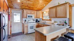 A kitchen with wooden cabinets, a microwave, stove, and a large island with stools. - Winnipesaukee Waterfront Home Sleeping for 8 (Moultonborough)