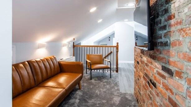 A modern loft-style room with a leather sofa, a wooden chair, and a brick wall.
