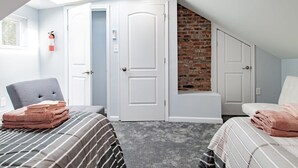 A bedroom with a sloped ceiling, a brick accent wall, a fire extinguisher, and two beds with folded towels.