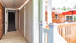 A narrow corridor with a door leading to a garage, a wooden fence, and a brick building in the background.