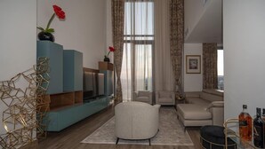 A modern living room with a sofa, armchairs, a coffee table, and a TV on a blue stand. There are decorative items like a vase with flowers and a geometric sculpture. - Africa's Touch & Leisure (Kigali)