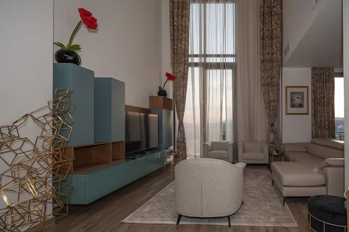 Ein modernes Wohnzimmer mit einer Couch, Sesseln, einem Couchtisch und einem blauen TV-Schrank. Es gibt Dekorationselemente wie eine Vase mit Blumen und eine geometrische Skulptur.