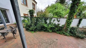 A paved patio area with a brick floor, a metal pole, and a white wall with ivy. - Hotel Jungmann (Saarlouis)