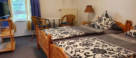 A room with two wooden beds, a small table, two wicker chairs, a lamp, and a television.
