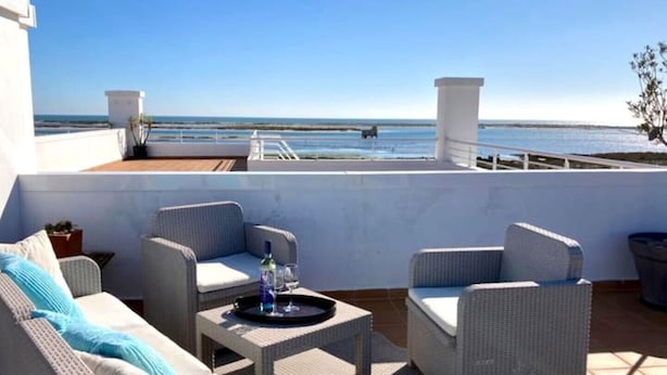 Een terras op het dak met rieten meubels, een kleine tafel met dienblad en uitzicht op zee.