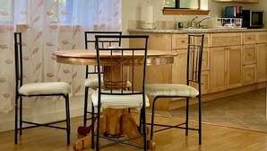 Un comedor con una mesa y sillas de madera, una cocina con armarios de madera, y una ventana con cortinas de encaje.