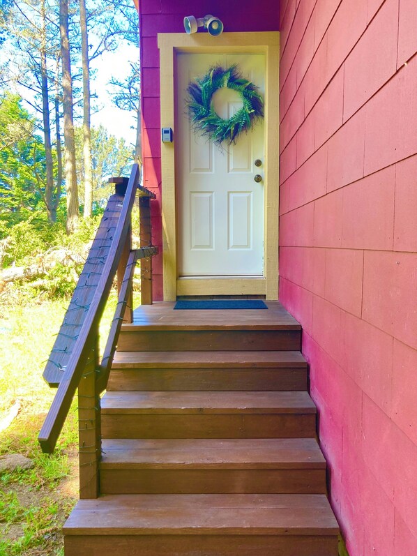 A wooden staircase leading to a white door with a green wreath, set against a pink wall.