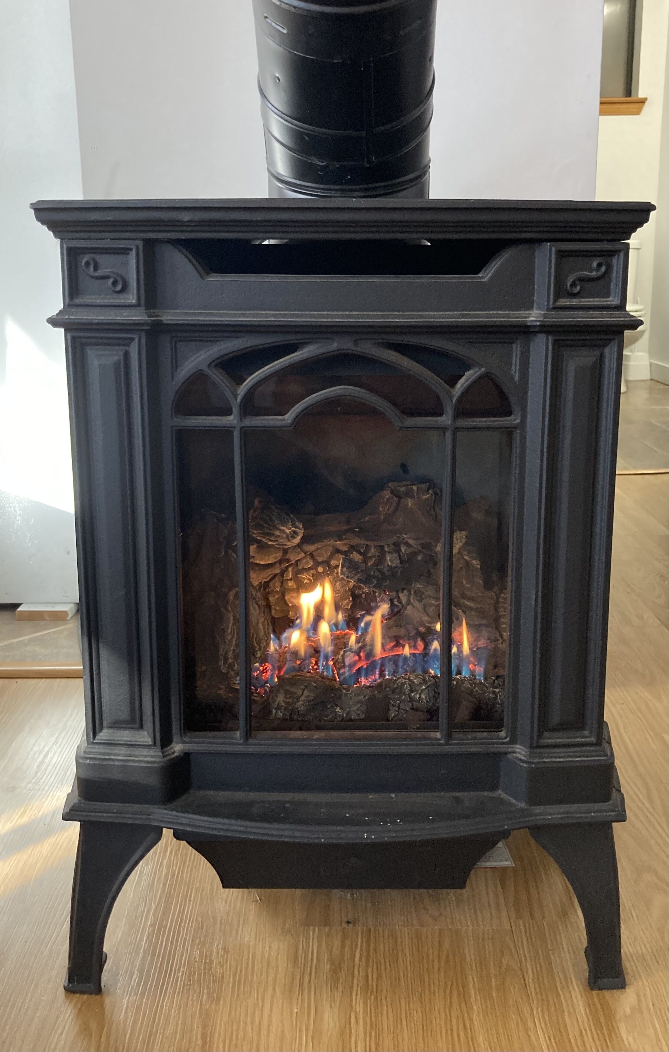 A black wood-burning stove with a glass front, a chimney above, and a wooden floor.