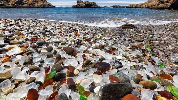 Una playa de guijarros con agua cristalina y afloramientos rocosos.