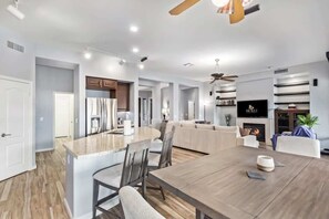 Un espacio habitable amplio con una gran mesa de madera para comer, un sofá y un televisor instalado en la pared.