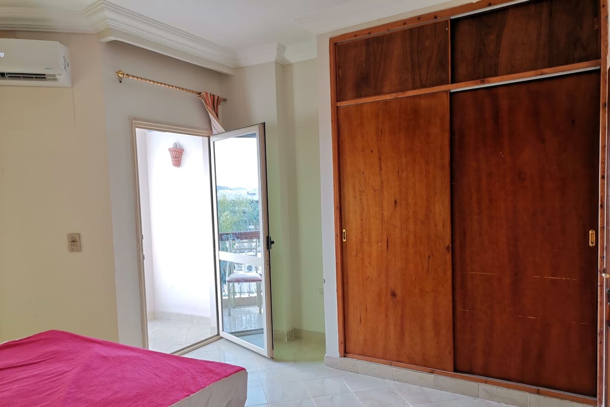 A room with a bed, a sliding wooden door, a balcony with a view, and an air conditioning unit.
