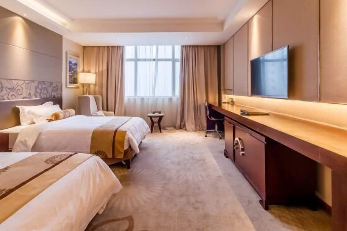 A hotel room with two beds, a desk, a TV, and a window with curtains.