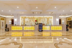 A hotel lobby with a reception desk, a patterned wall, and a polished floor. - Fuxin International Hotel (Shangrao)