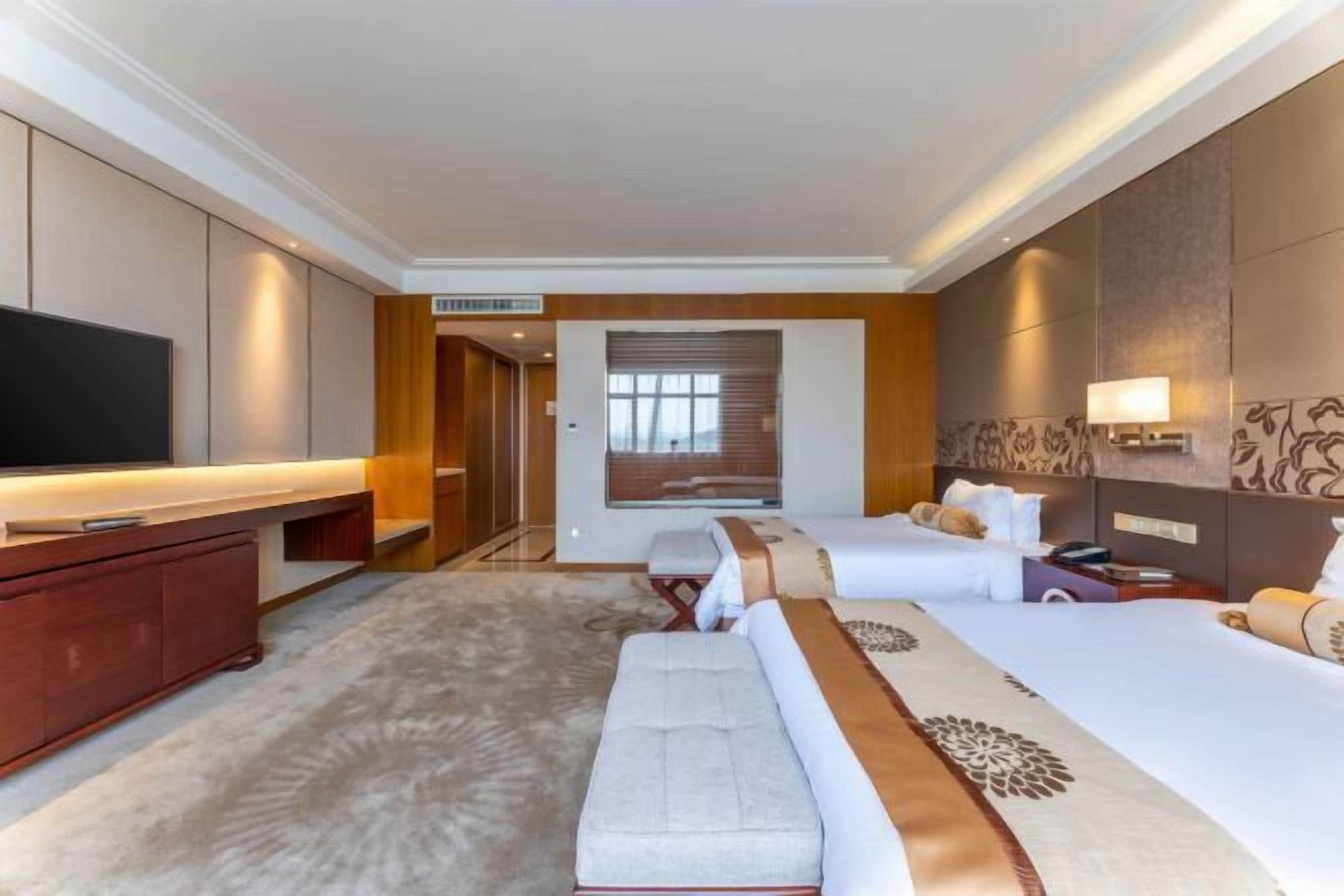 A hotel room with a large flat-screen TV, a sofa, a bed, and a desk with a lamp.
