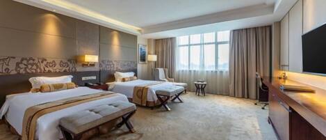 Quarto de hotel com duas camas, uma escrivaninha, uma televisão e uma janela grande.