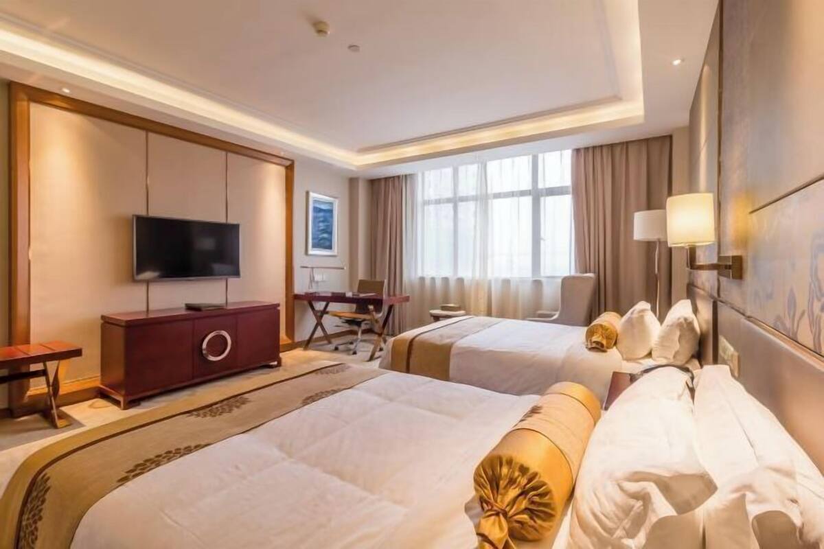 A hotel room with two beds, a TV, a desk, and a window with curtains.