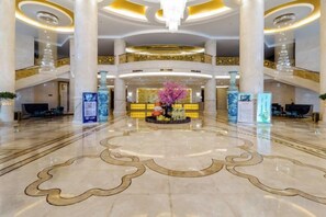 A spacious lobby with a central floral arrangement, multiple reception desks, and a grand staircase. - Fuxin International Hotel (Shangrao)