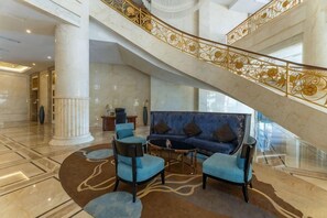 A lobby with a grand staircase, a blue sofa, and a coffee table. - Fuxin International Hotel (Shangrao)