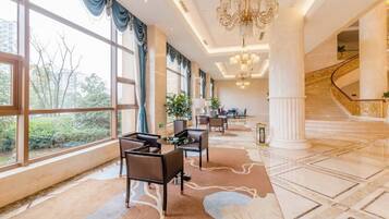 Un amplio vestíbulo de hotel con una escalera monumental, ventanas grandes y un candelabro.