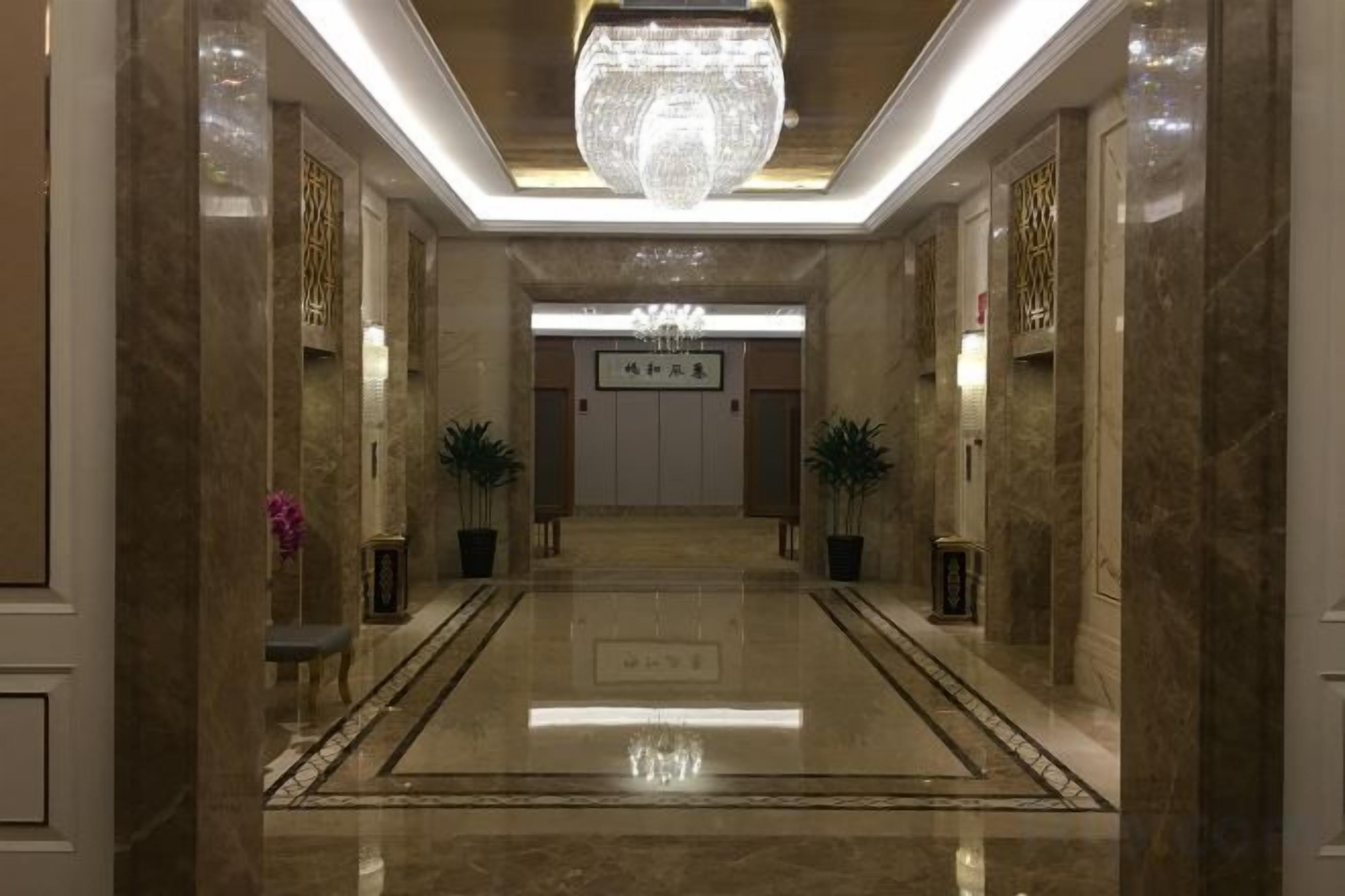 A hotel lobby with a marble floor, a chandelier, and a reception desk.