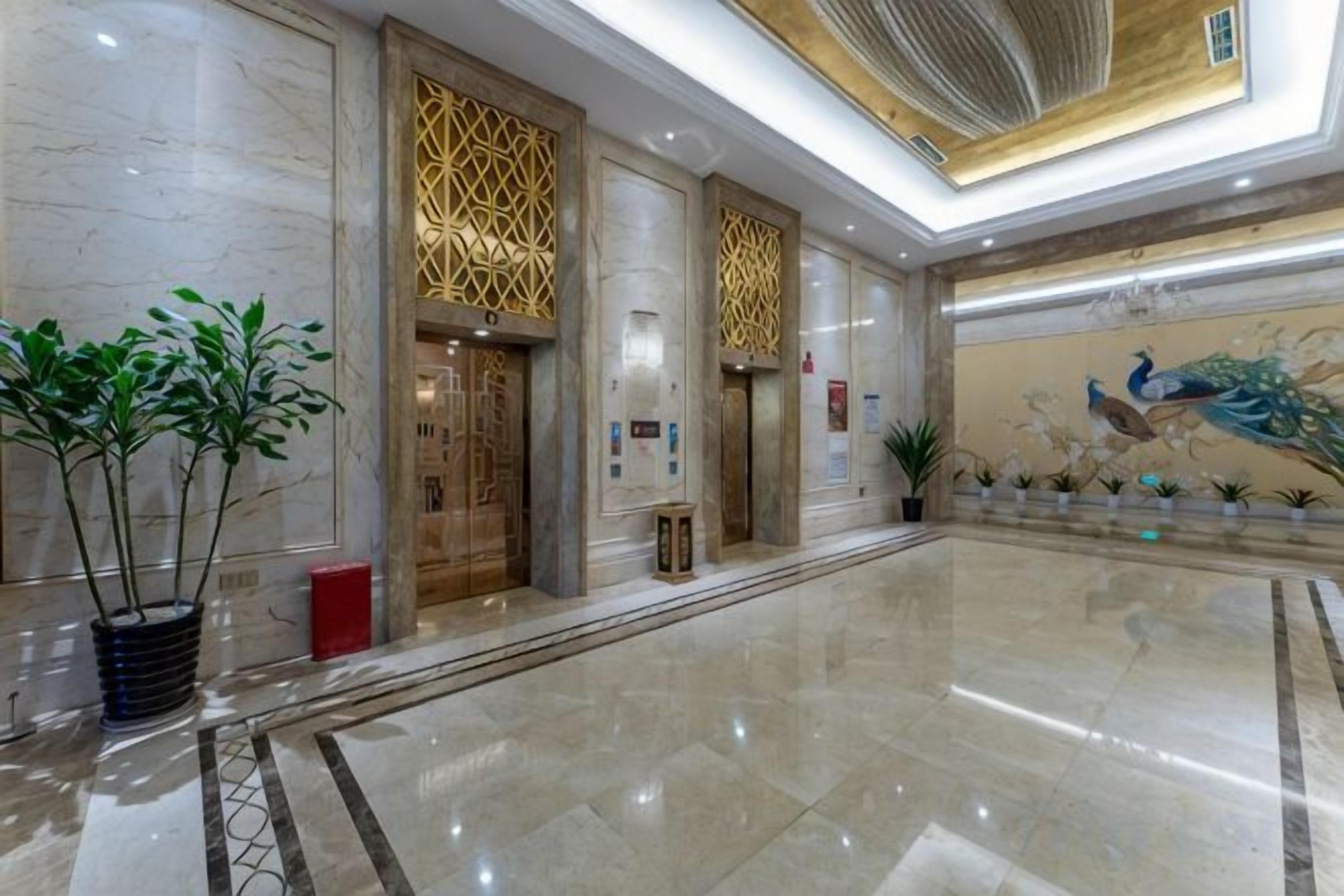 A spacious lobby with marble flooring, decorative wall panels, and a peacock mural.