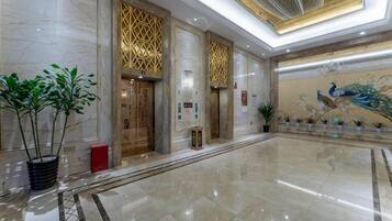A spacious lobby with marble flooring, decorative wall panels, and a peacock mural.