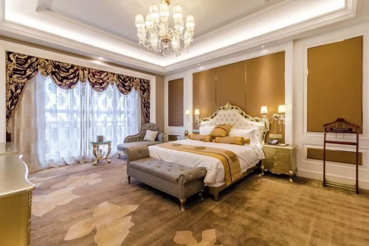 A luxurious bedroom with a large bed, a chaise lounge, and a chandelier.