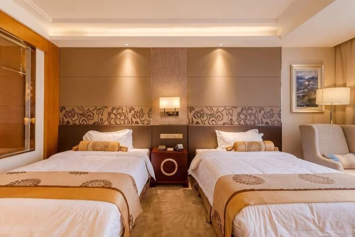 A hotel room with two beds, a nightstand, a lamp, and a chair.