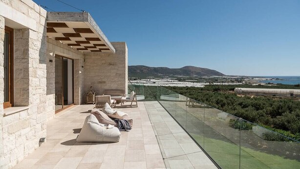 A modern outdoor lounge area with stone walls, a glass balustrade, and a view of the coastline. - Casa le Cicale the top villa in Falasarna,Basketbal,pool,BBQ (Phalasarna)