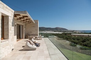 A modern outdoor lounge area with stone walls, a glass balustrade, and a view of the coastline. - Casa le Cicale the top villa in Falasarna,Basketbal,pool,BBQ (Phalasarna)