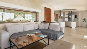 A modern living room with a sofa, coffee table, and a view of a kitchen and outdoor area. - Casa le Cicale the top villa in Falasarna,Basketbal,pool,BBQ (Phalasarna)