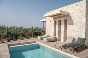 Uma área de piscina no terraço, com paredes de pedra, espreguiçadeiras e vista para a paisagem.